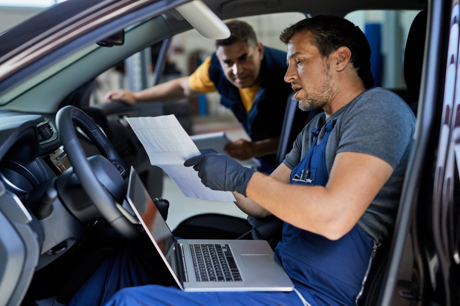Auto repairman talking to his colleague while running car diagnostic and  analyzing data in a workshop.